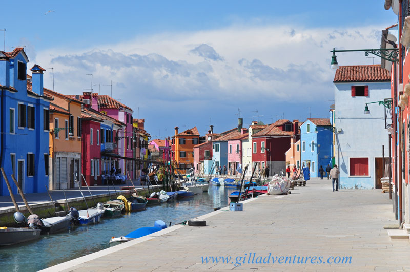 Burano, Italy boats in the canal Burano, Italy with colorful buildings, boats in the canal, and storm clouds in the distance.